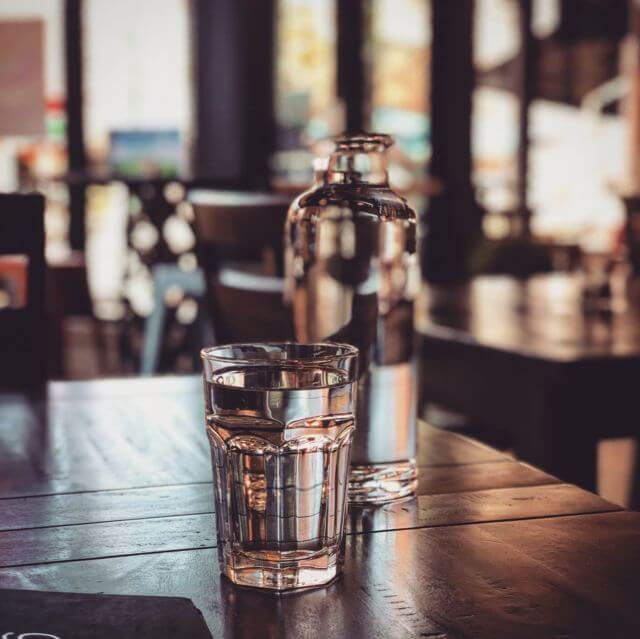 glass bottle and cup full of water placed on top of a table
