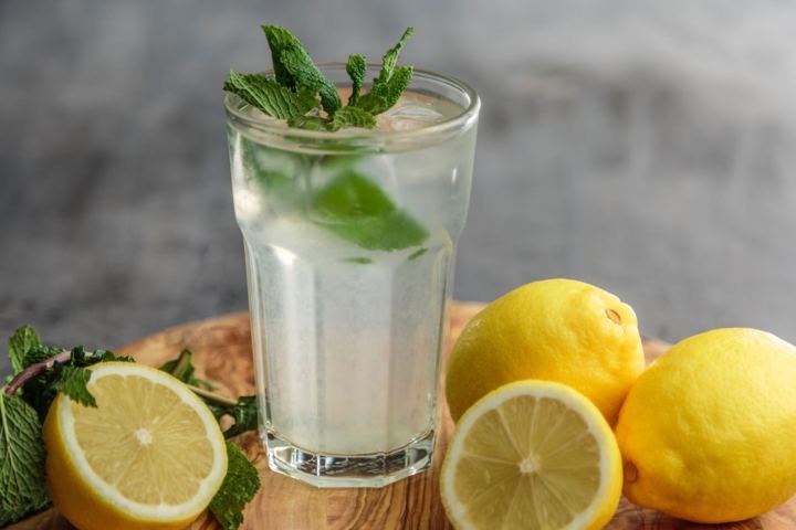 glass of water with mint leaves with lemons arranged around it
