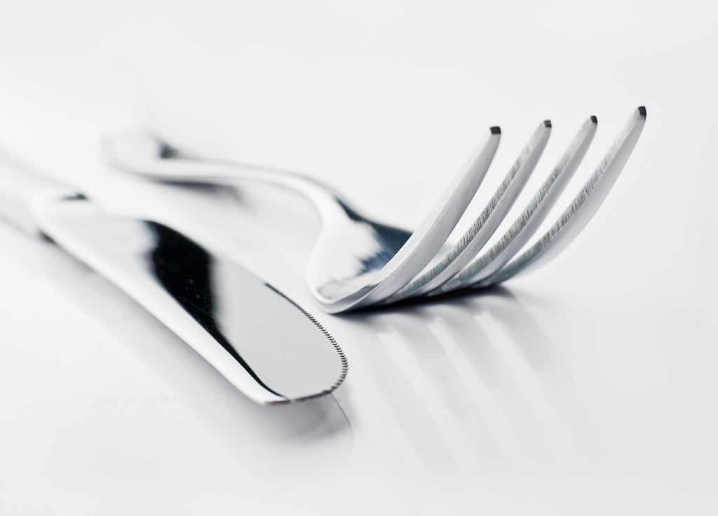 silver table knife and fork placed on a white surface