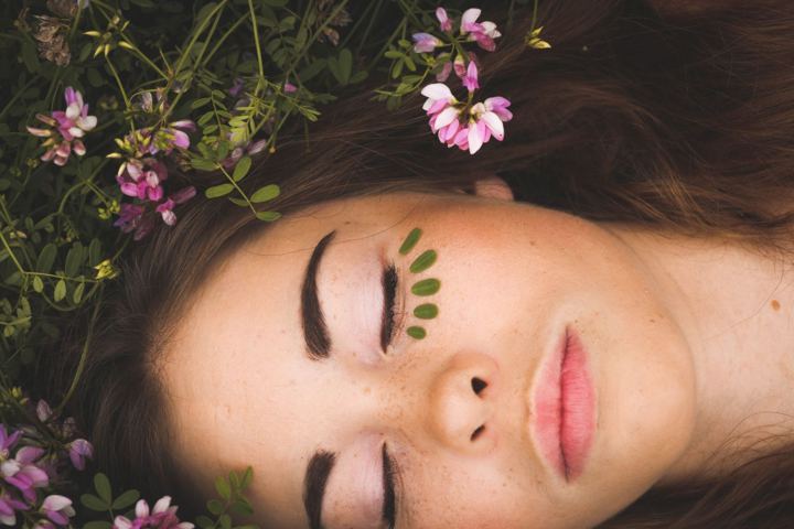 woman with tiny leaves arranged under her eyes lying down on a field of grass and flowers
